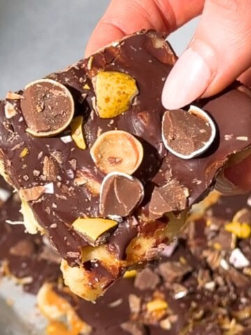 Frozen peanut butter banana bark topped with chocolate and crushed mini eggs, held in hand.