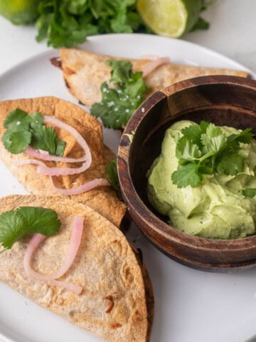 Chicken mini tacos on corn tortillas topped with pickled onions and fresh cilantro, served with a bowl of creamy guacamole.