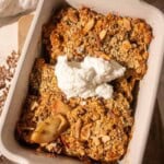 Healthy apple crumble with baked apples and oat topping, served in a white dish with a dollop of Greek yogurt and sprinkled nuts