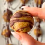 Close up of a no-bake peanut butter protein ball without protein powder drizzled with chocolate held between fingers