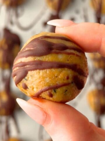 Close up of a no-bake peanut butter protein ball without protein powder drizzled with chocolate held between fingers