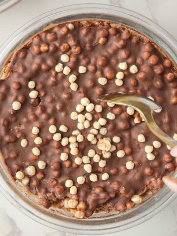 Chocolate protein overnight oats topped with a smooth, crackable chocolate shell broken with a spoon in a glass bowl