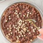 Chocolate protein overnight oats topped with a smooth, crackable chocolate shell broken with a spoon in a glass bowl
