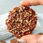 Chocolate quinoa crisp coated in dark chocolate and topped with puffed quinoa, held between fingers to show the crunchy texture. Homemade chocolate quinoa crisps made with puffed quinoa and melted chocolate.