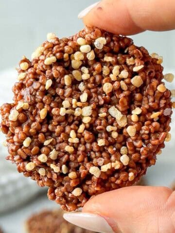 Chocolate quinoa crisp coated in dark chocolate and topped with puffed quinoa, held between fingers to show the crunchy texture. Homemade chocolate quinoa crisps made with puffed quinoa and melted chocolate.