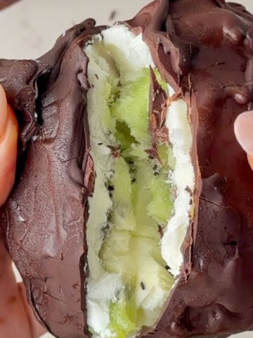 Close-up of a chocolate-coated frozen yogurt kiwi bite being pulled apart to reveal a creamy Greek yogurt filling and fresh kiwi slices inside