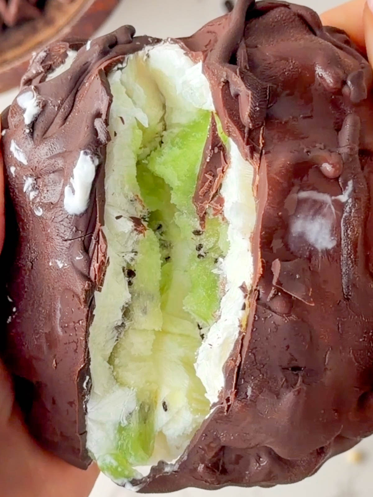 Close-up of a chocolate-coated frozen yogurt kiwi bite being pulled apart to reveal a creamy Greek yogurt filling and fresh kiwi slices inside