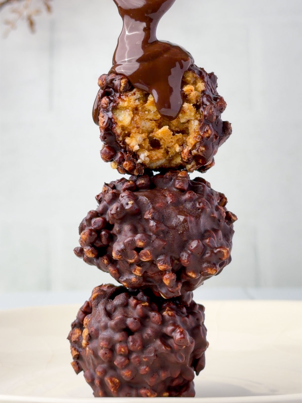Chocolate peanut butter protein balls stacked with a gooey chocolate drizzle pouring over the top, showing the crispy rice texture inside.