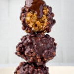 Chocolate peanut butter protein balls stacked with a gooey chocolate drizzle pouring over the top, showing the crispy rice texture inside.