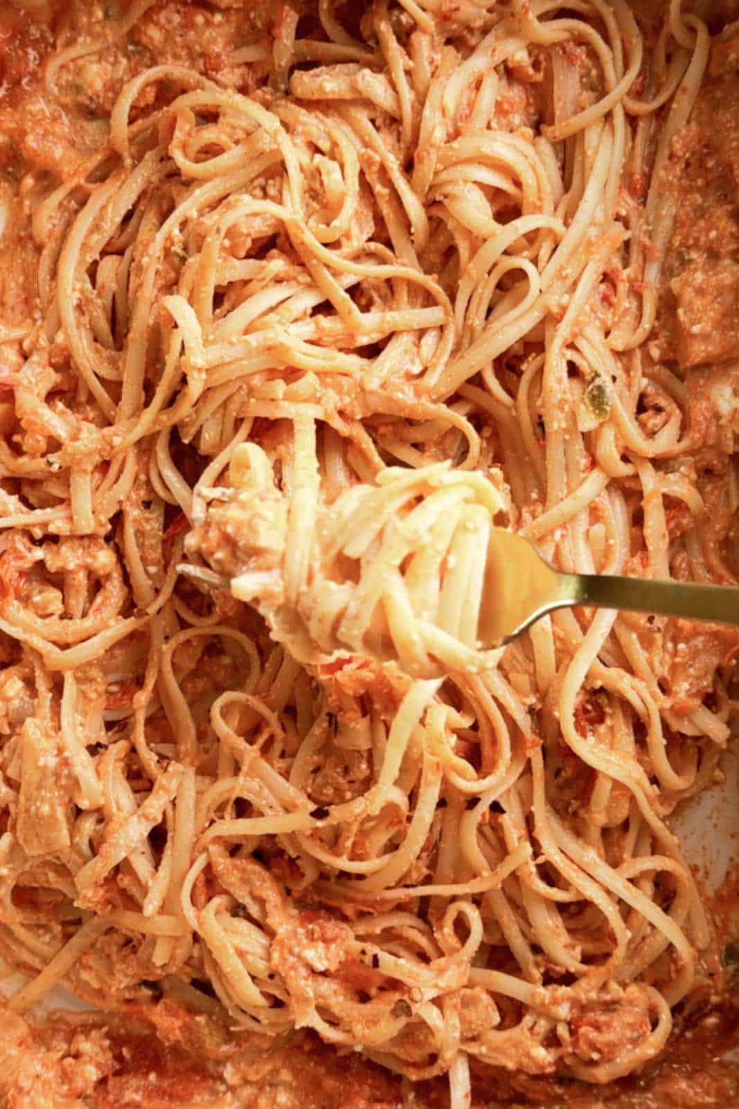 Close-up of creamy spicy feta pasta with spaghetti coated in a rich tomato and feta cheese sauce. A fork twirls a bite of pasta from the baking dish.