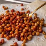 Spicy roasted chickpeas with harissa served on parchment paper with a gold spoon. The crispy chickpeas are coated in smoky harissa paste, giving them a rich red color and bold flavor.