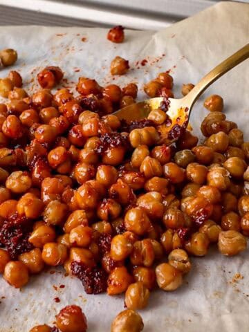 Spicy roasted chickpeas with harissa served on parchment paper with a gold spoon. The crispy chickpeas are coated in smoky harissa paste, giving them a rich red color and bold flavor.