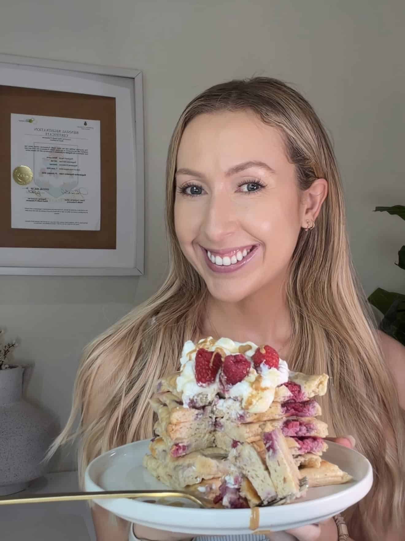 Registered dietitian Maria Lucey holding a plate of sheet pan protein pancakes topped with whipped yogurt, fresh raspberries, and a drizzle of honey.
