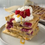 Stack of sheet pan protein pancakes filled with raspberries and topped with whipped yogurt, fresh raspberries, and a drizzle of honey.