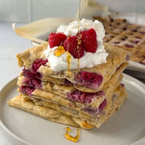 Stack of sheet pan protein pancakes filled with raspberries and topped with whipped yogurt, fresh raspberries, and a drizzle of honey.