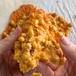 Cheesy Chickpea Chips held in hands, showing a crispy, golden baked chickpea and cheese cracker with a crunchy texture.