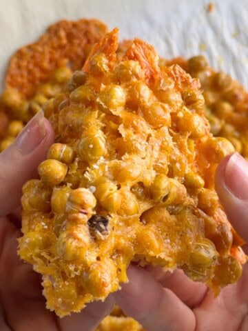Cheesy Chickpea Chips held in hands, showing a crispy, golden baked chickpea and cheese cracker with a crunchy texture.