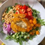 Chickpea and halloumi salad with crispy golden halloumi, chickpeas, quinoa, arugula, cucumber, red onion and colorful cherry tomatoes in a white bowl.