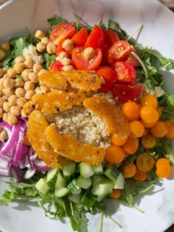 Chickpea and halloumi salad with crispy golden halloumi, chickpeas, quinoa, arugula, cucumber, red onion and colorful cherry tomatoes in a white bowl.