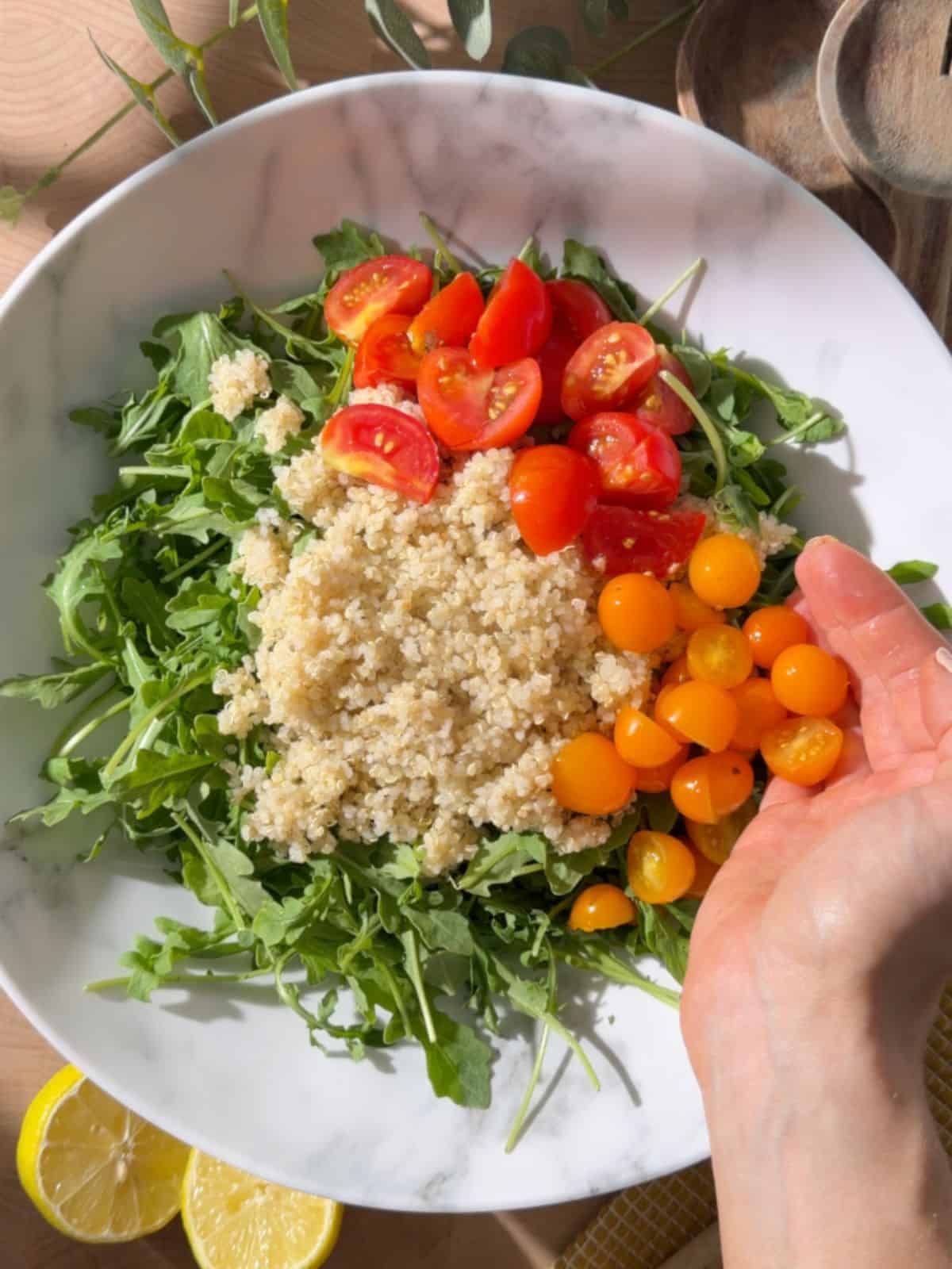 Chickpea and halloumi salad being assembled with arugula, cooked quinoa, red and yellow cherry tomatoes, and lemon wedges.