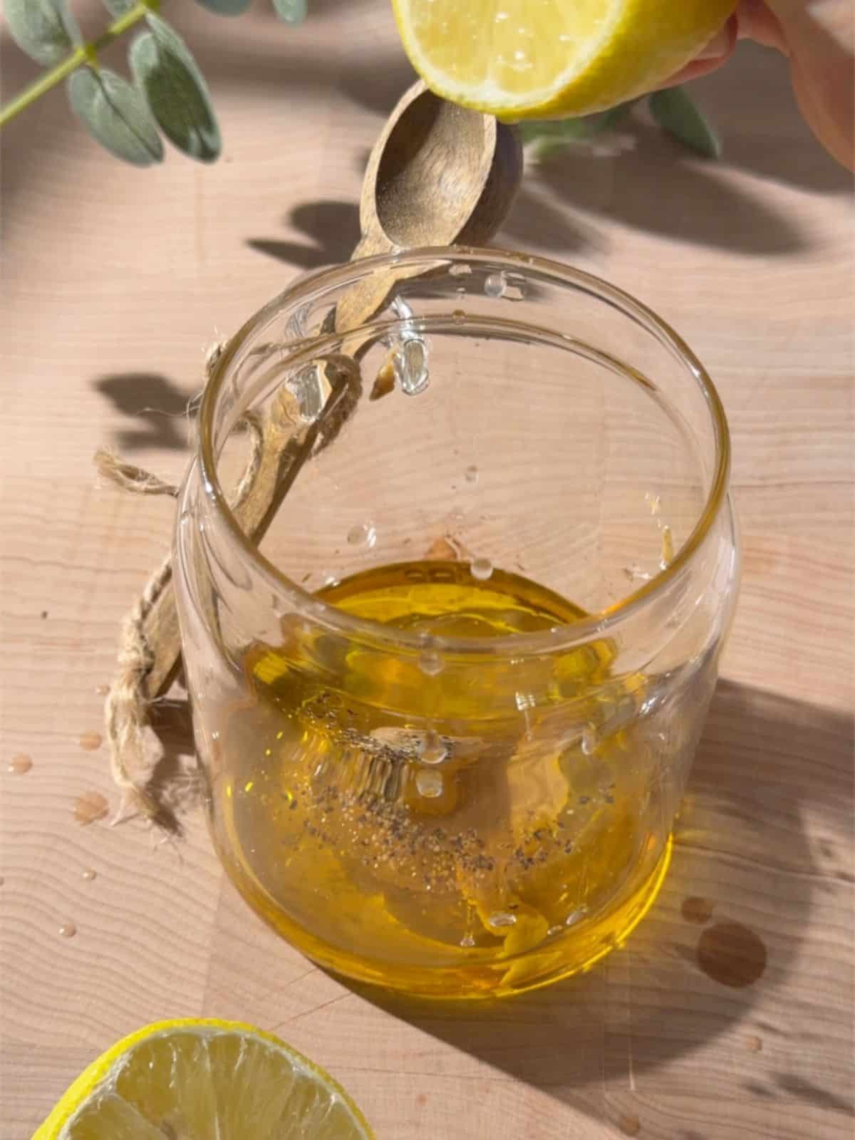Lemon being squeezed into a glass jar with olive oil, pepper and dressing ingredients for chickpea and halloumi salad.