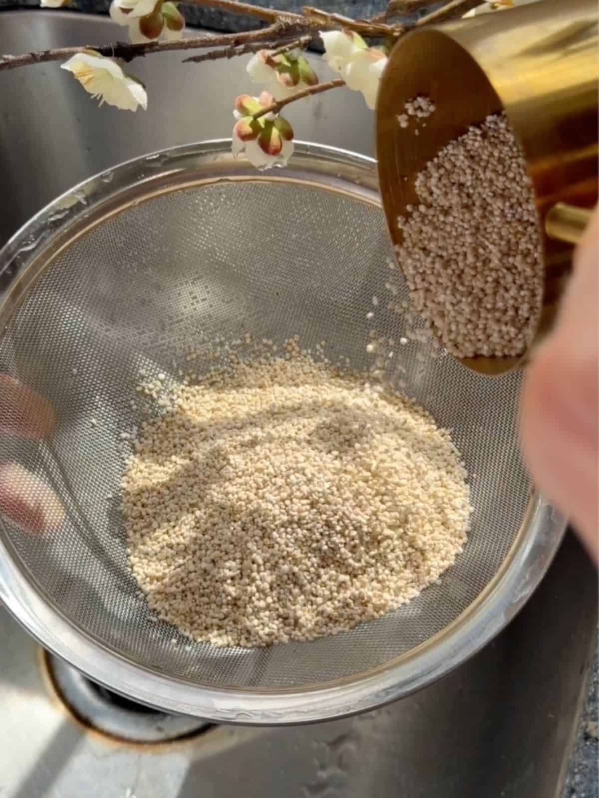 Quinoa being poured into a fine mesh sieve over a sink before rinsing for chickpea and halloumi salad.