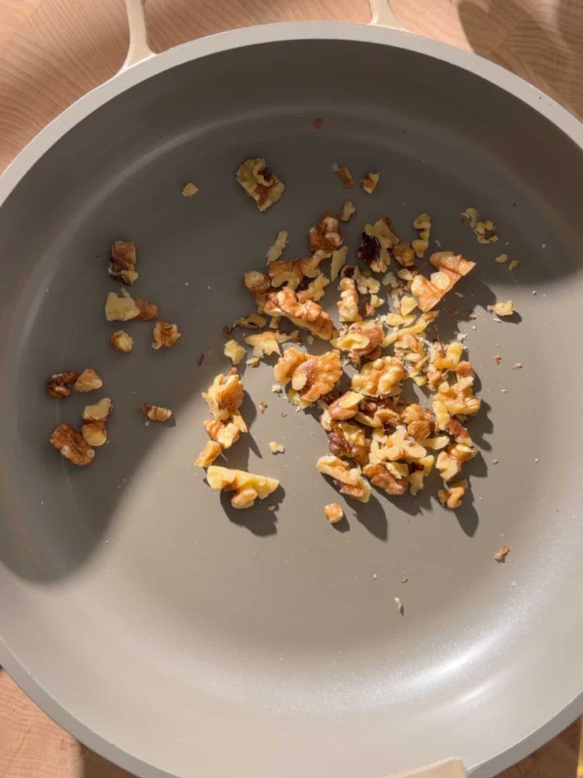 Chopped walnuts being toasted in a frying pan for chickpea and halloumi salad.