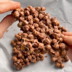 Hands breaking apart a piece of chocolate chickpea bark made with crispy roasted chickpeas, melted chocolate and a sprinkle of flaky sea salt.