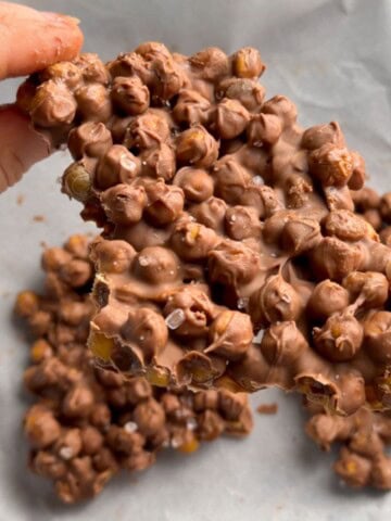 Hands breaking apart a piece of chocolate chickpea bark made with crispy roasted chickpeas, melted chocolate and a sprinkle of flaky sea salt.