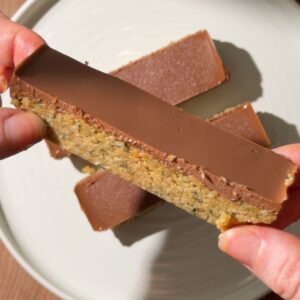 Close-up of a no-bake chocolate peanut butter hemp seed bar showing its fudgy hemp and oat base with a smooth chocolate topping.