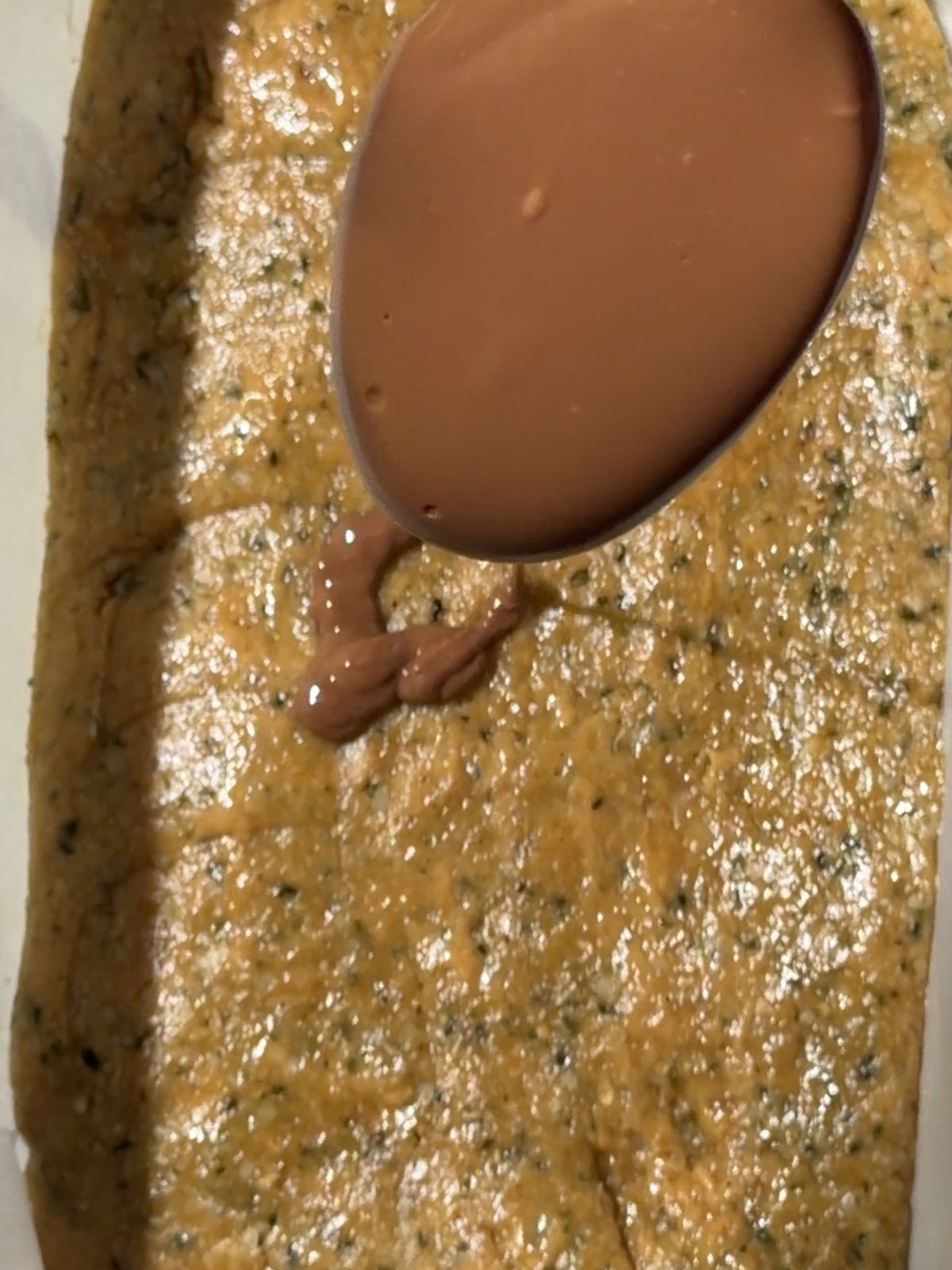 Pouring melted chocolate over the hemp seed and peanut butter base in a loaf pan.