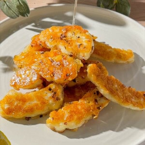 Hot honey halloumi with golden pan-fried halloumi pieces drizzled with honey and chilli flakes on a plate.