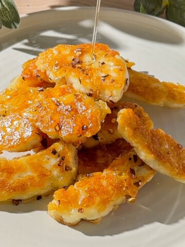 Hot honey halloumi with golden pan-fried halloumi pieces drizzled with honey and chilli flakes on a plate.