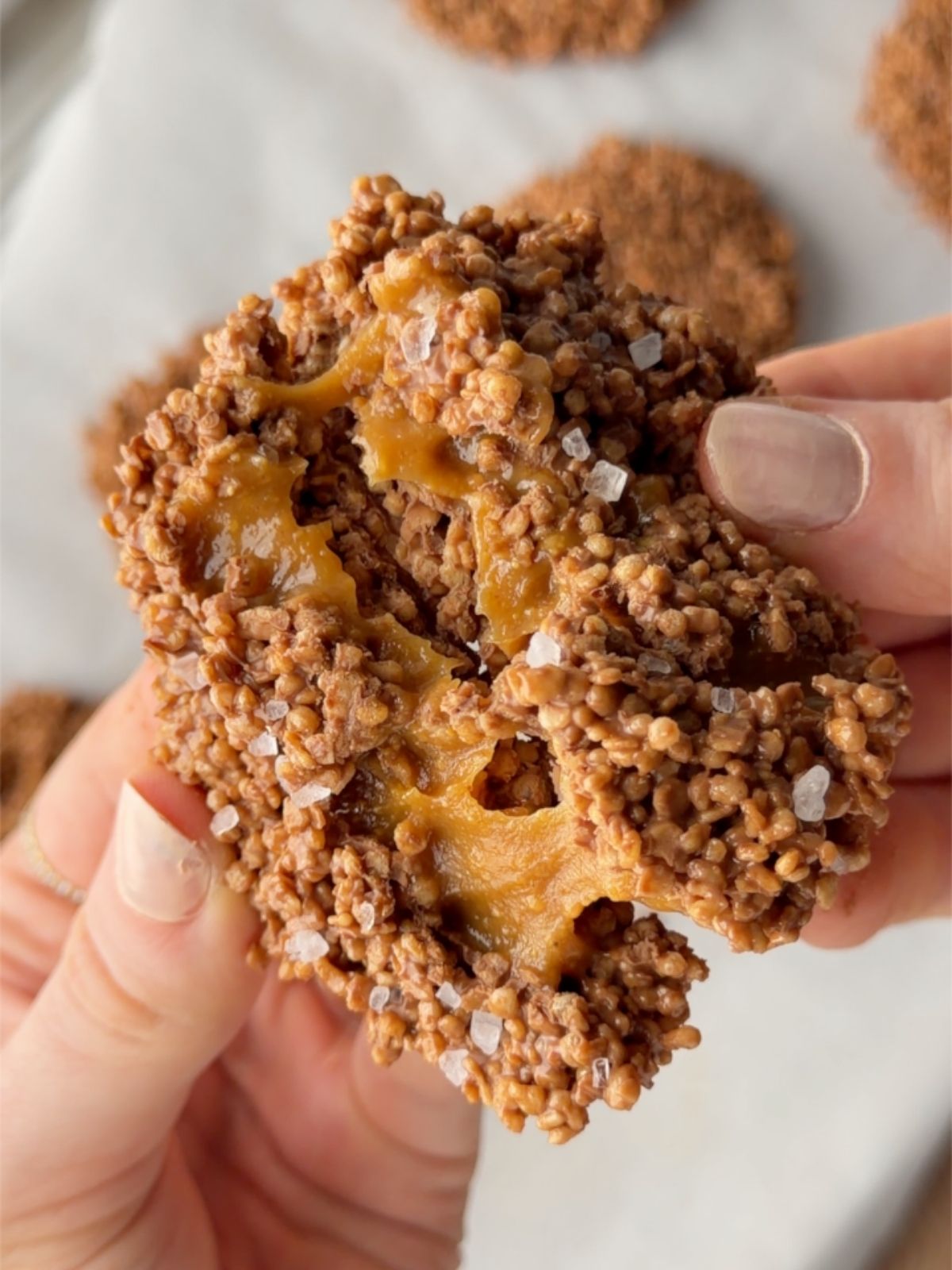 Salted caramel chocolate quinoa crisps broken in half to show the chewy caramel center and flaky sea salt topping.