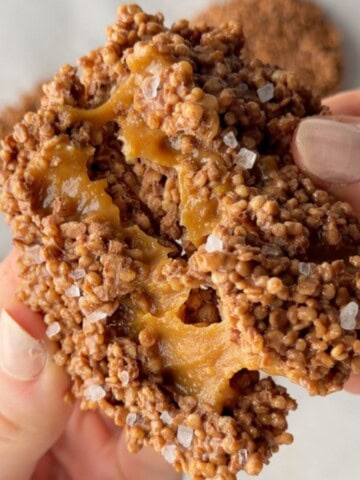 Salted caramel chocolate quinoa crisps broken in half to show the chewy caramel center and flaky sea salt topping.