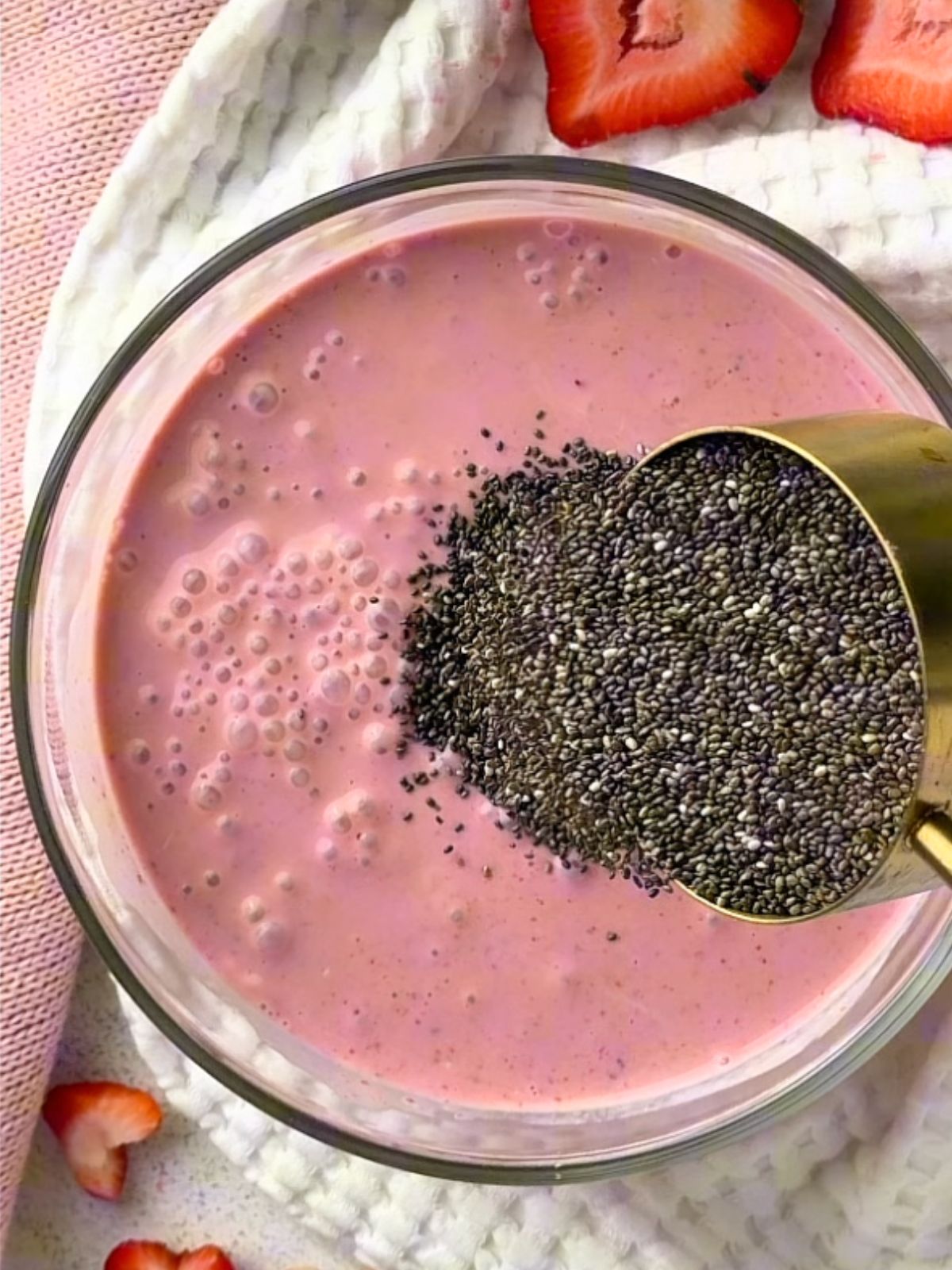 Chia seeds being poured into a bowl of blended strawberry yogurt mixture for strawberry chia pudding.