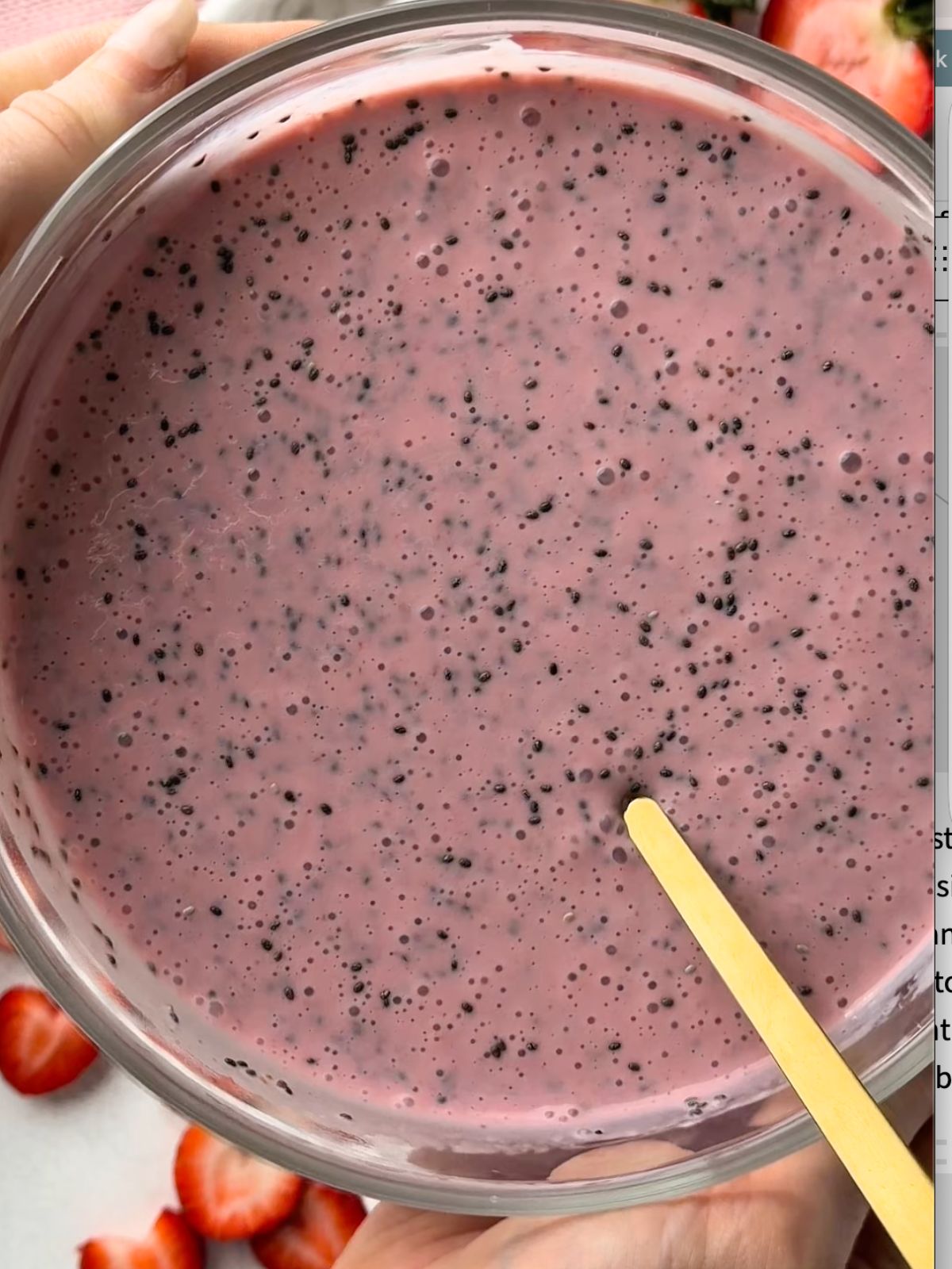 Pink strawberry chia pudding mixture in a glass bowl after the chia seeds have been stirred through.