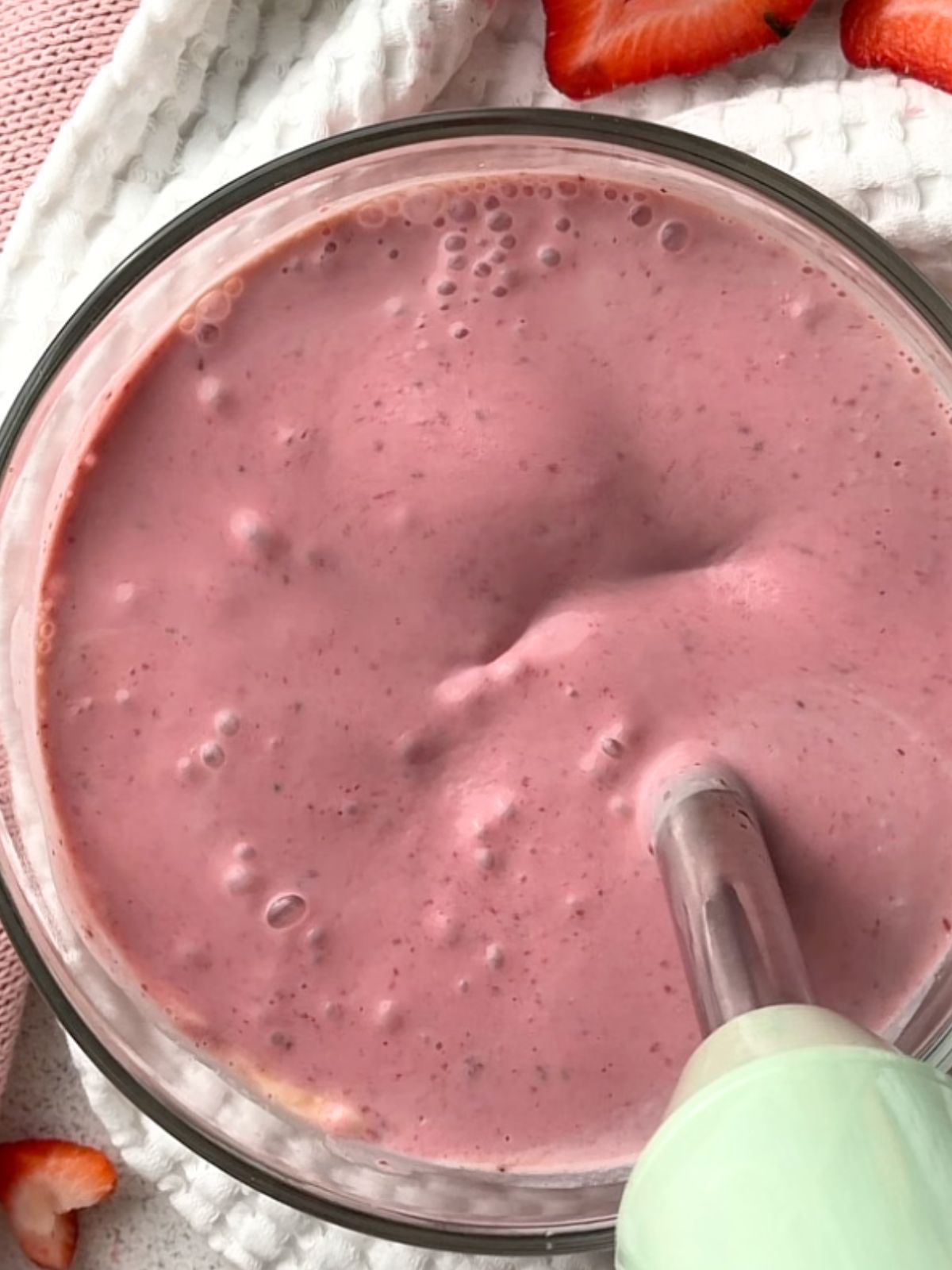 An immersion blender blending a creamy pink strawberry yogurt mixture for homemade strawberry chia pudding.