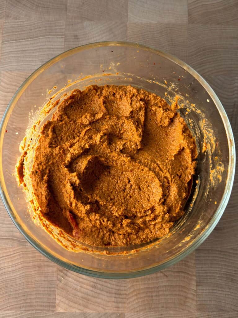 Finished muhammara recipe in a glass bowl showing the thick, scoopable roasted red pepper and walnut dip texture.