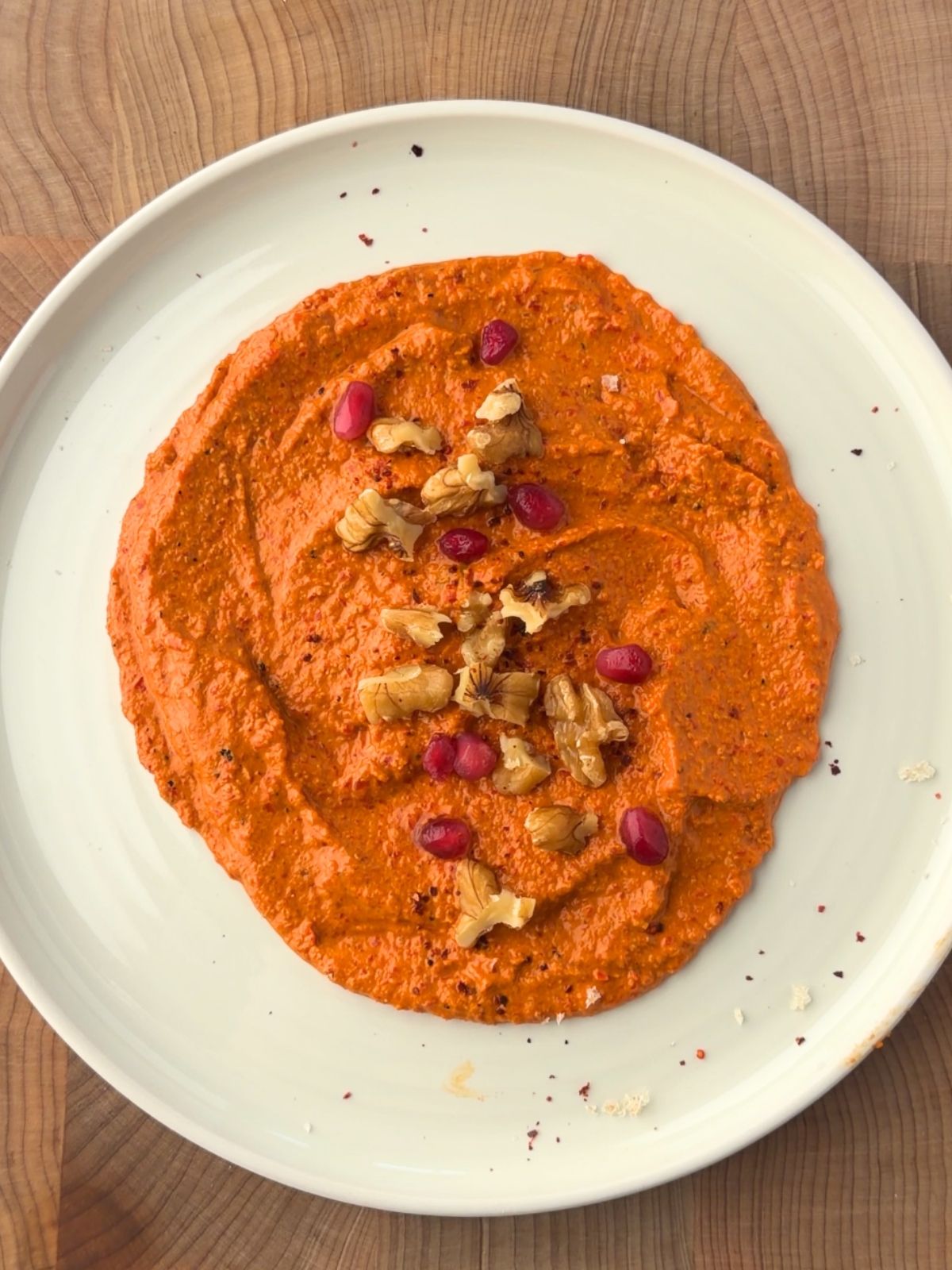 Muhammara recipe served on a plate and topped with chopped walnuts and pomegranate seeds.