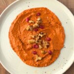 Muhammara recipe served on a plate and topped with chopped walnuts and pomegranate seeds.