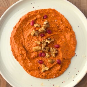 Muhammara recipe served on a plate and topped with chopped walnuts and pomegranate seeds.
