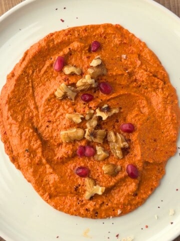 Muhammara recipe served on a plate and topped with chopped walnuts and pomegranate seeds.