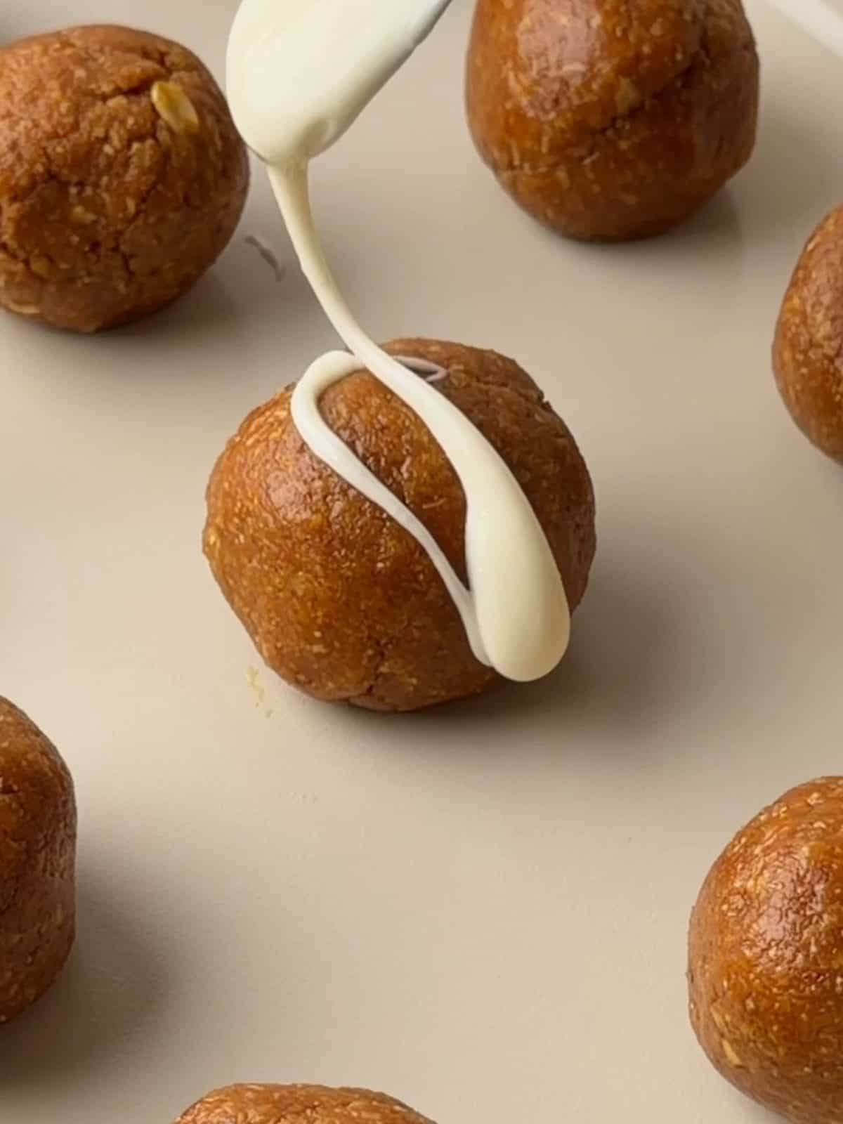 Pumpkin protein balls being drizzled with melted white chocolate before chilling.