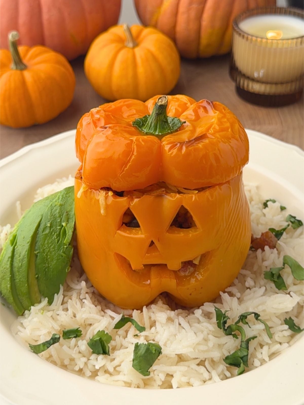 Jack o lantern stuffed pepper filled with ground turkey, topped with melted cheese, and served over rice with sliced avocado and fresh cilantro.