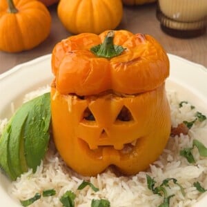 Jack o lantern stuffed pepper filled with ground turkey, topped with melted cheese, and served over rice with sliced avocado and fresh cilantro.