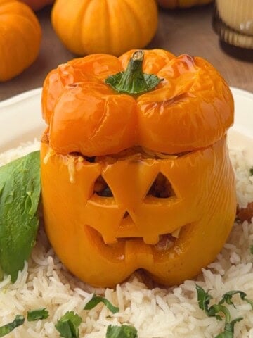 Jack o lantern stuffed pepper filled with ground turkey, topped with melted cheese, and served over rice with sliced avocado and fresh cilantro.