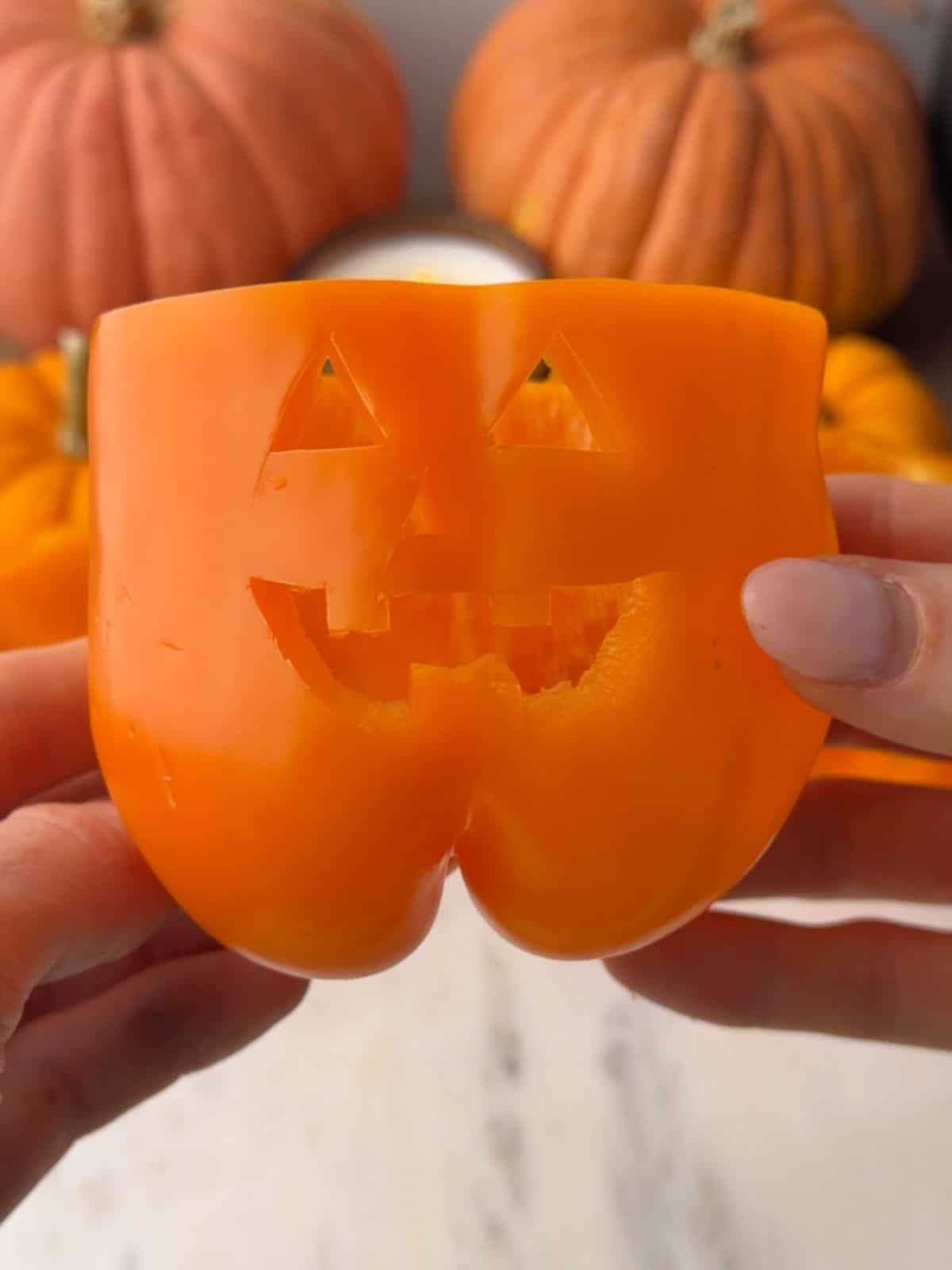 Orange bell pepper carved with a jack-o'-lantern face, ready to be filled with a savory turkey mixture.
