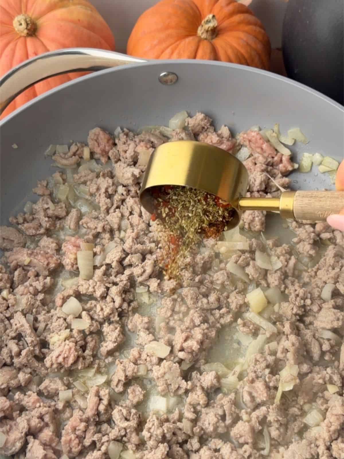 Adding herbs and spices to a skillet of ground turkey and diced onions for Halloween stuffed peppers.