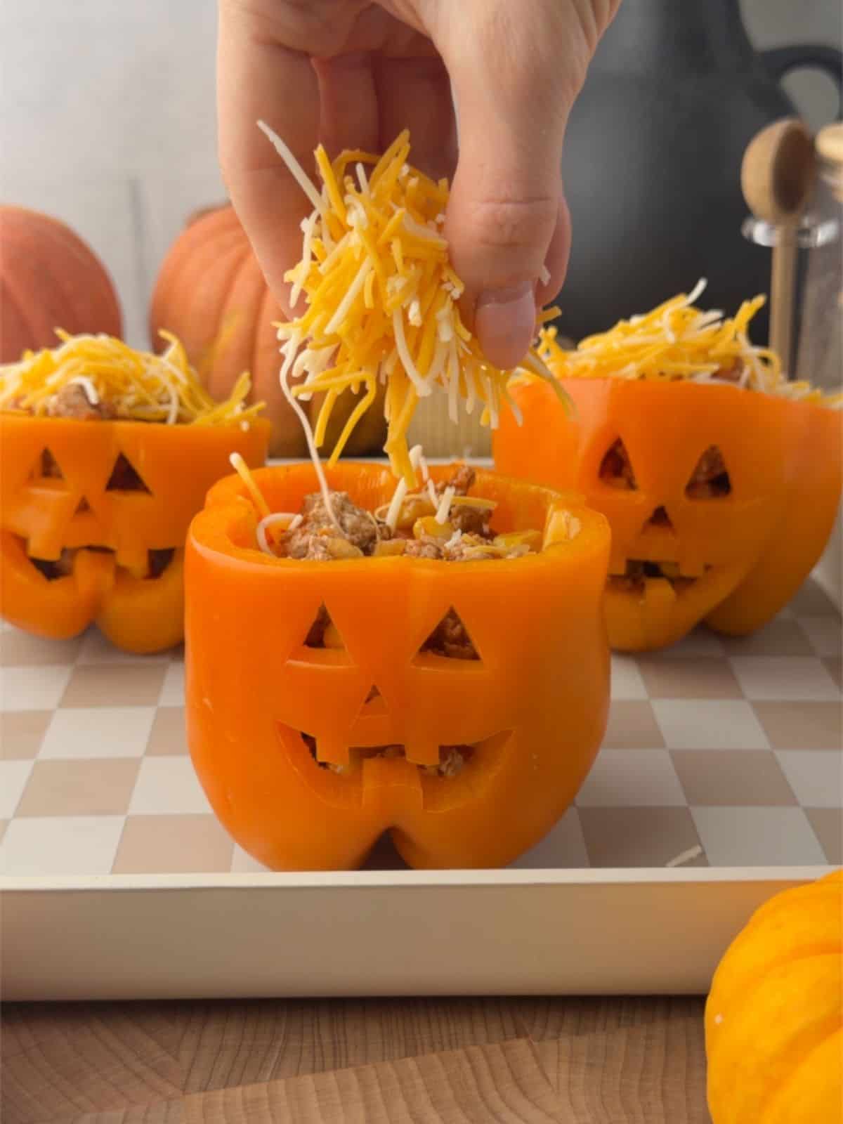 Sprinkling shredded cheese over jack-o'-lantern stuffed peppers filled with ground turkey, black beans, and corn.